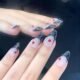 Model wearing grey and black glitter French press-on nails with red rhinestones