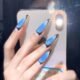 Fashion model showcasing Lavara blue black press-on nails with sleek stiletto design