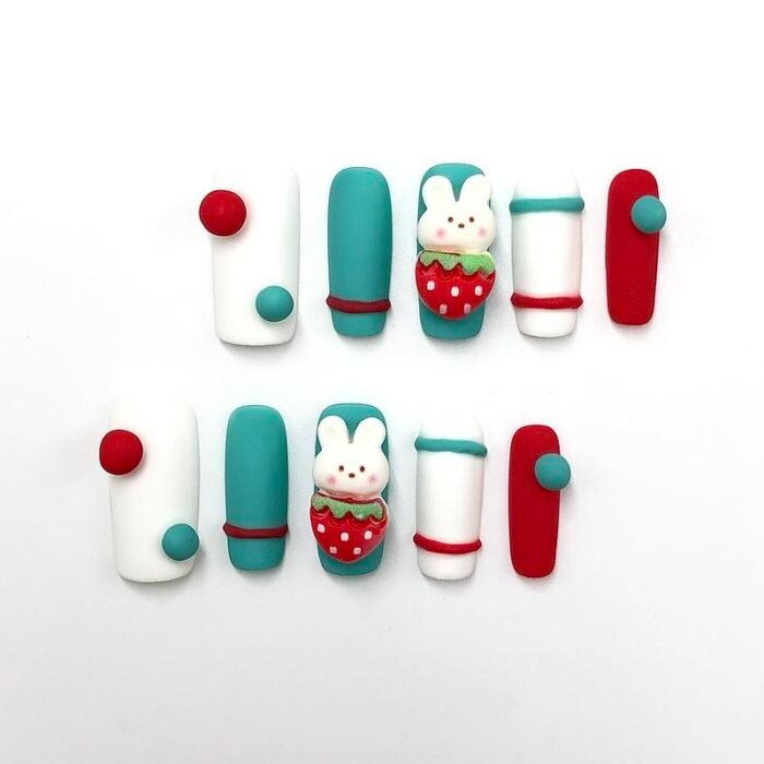 Front view of artistic cute bunny strawberry press-on nails with 3D embellishments in red, white, and teal